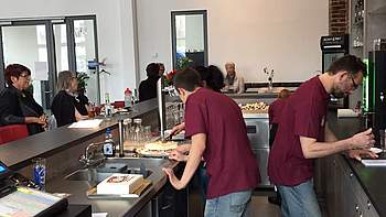 Zwei Menschen mit roten T-Shirts arbeiten hinter der Theke einer Cafeteria